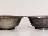 two metal bowls sitting on top of a white surface next to each other