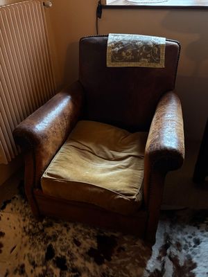 un fauteuil en cuir marron, avec un coussin posé dessus, devant une fenêtre