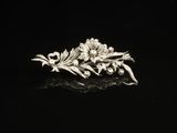 a silver broochle with flowers and leaves on a black surface