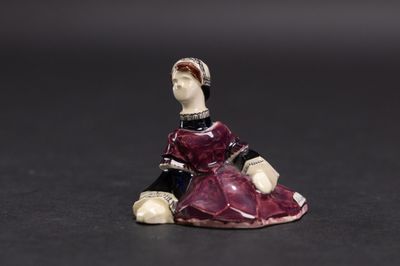 une vieille figurine représentant une femme en robe rouge, assise sur une surface noire