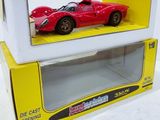 une petite voiture rouge dans une boîte jaune posée sur une surface blanche