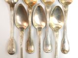 six silver spoons are lined up in a row on a white surface