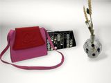 a pink purse with a red strap next to a vase with flowers