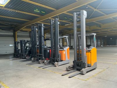 Plusieurs chariots élévateurs sont garés dans un grand entrepôt, avec un garage en arrière-plan.