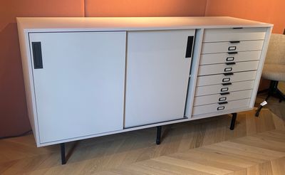 a white cabinet with drawers and a chair in the corner