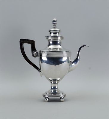 une théière ancienne en argent, avec une anse noire, posée sur un socle