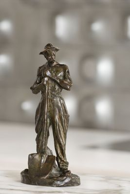 une statue en bronze représentant un homme tenant une pelle, posée sur une table
