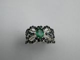 a close up of a ring with a green stone surrounded by black diamonds