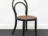 une image représentant une chaise noire avec une assise en osier, posée sur un sol recouvert de moquette