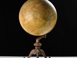 an antique globe on a tripod stand against a black background