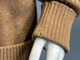 the arm of a mannequin wearing a brown sweater and gloves