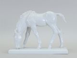 une statue blanche représentant un cheval en train de brouter, posée sur une surface blanche