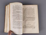 someone is holding an open book in their hand on a gray surface