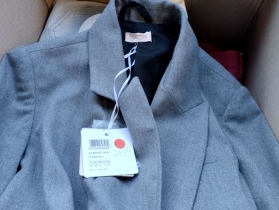 un manteau gris muni d'une étiquette, posé dans une boîte