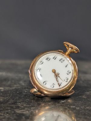 une petite montre de poche en or posée sur une surface en marbre