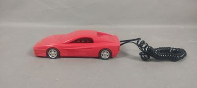 une petite voiture rouge avec un cordon qui y est attaché, posée sur une surface blanche