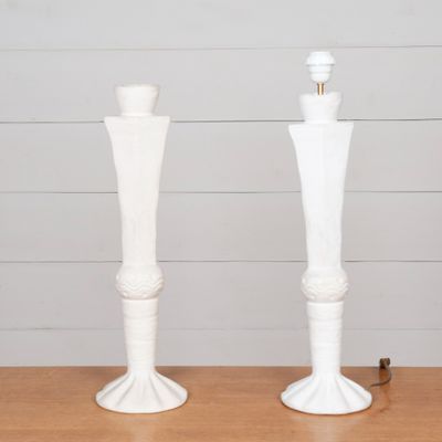 Deux bougies blanches sont posées sur une table en bois, avec un mur blanc en arrière-plan.