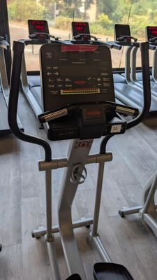 a row of tread machines in a gym with a view of trees