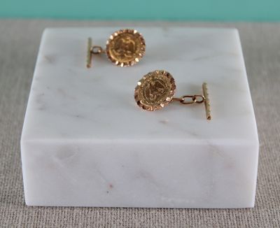 a close up of a pair of gold cufflinks on a marble block