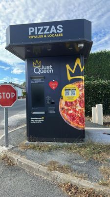a pizza kiosk on the side of the road next to a stop sign