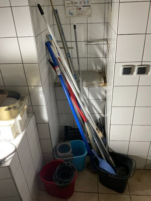 Plusieurs balais et seaux sont posés dans une salle de bains, à côté des toilettes.