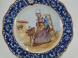 a blue and white plate with a picture of a woman sitting on a chair
