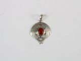 a close up of a silver pendant with a red stone