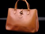 tan leather handbag with gold hardware on a black background