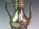 a silver tea pot sitting on a stand on a table