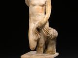 une statue antique représentant un homme tenant un bouclier, posée sur un socle