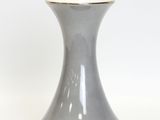 a gray vase with a gold rim sitting on a white surface