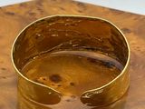 gold plated cuff bracelet on a wooden table with a white background