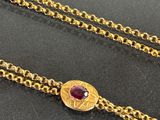 a close up of a gold chain with a red stone on it