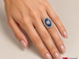 woman ' s hand with a blue and white diamond ring on it