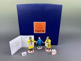 three figurines of people in yellow and blue outfits stand in front of a blue box