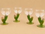 quatre verres à vin ornés de tiges et de feuilles vertes, posés sur un fond beige