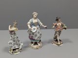 trois figurines en porcelaine représentant des femmes en robe et chapeau, posées sur une table