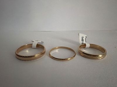three gold wedding rings on a white surface