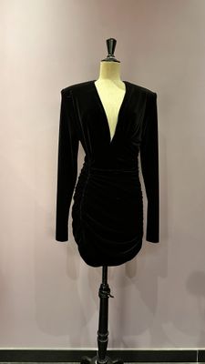 une robe en velours noir posée sur un mannequin devant un mur rose