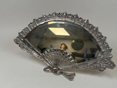 un miroir argenté en forme d'éventail posé sur une table blanche