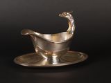 a silver sauce boat on a silver plate on a black background