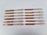 six couteaux argentés sont alignés sur une surface blanche