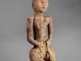 a statue of a man sitting on a stool with a hat on his head