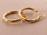 two gold hoop earrings on a beige surface