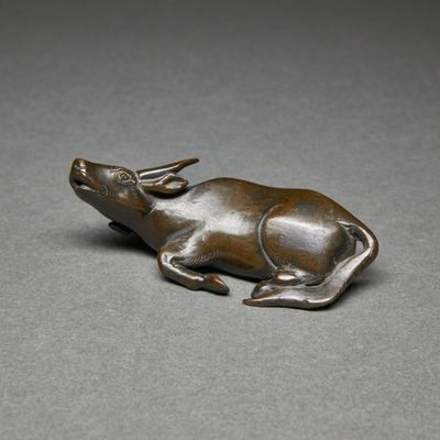 bronze figurine of a bull lying down on a gray surface