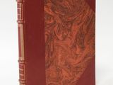 an old book with a red cover sitting on top of a white surface