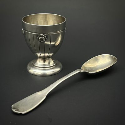 une tasse en argent et une cuillère posées sur une table noire