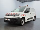 La camionnette blanche est garée dans une grande pièce ; elle porte une bande rouge et blanche sur le côté.
