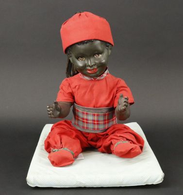 a black doll with a red hat sitting on a white cushion