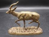 statue en bronze représentant une gazelle courant sur un rocher posé sur un fond noir